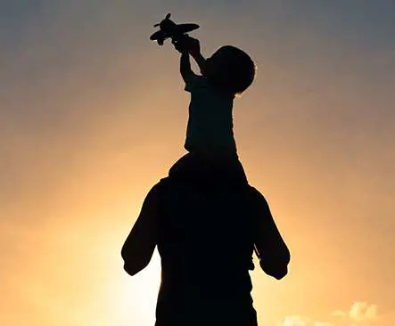 Child sitting on a parents shoulders holding a toy